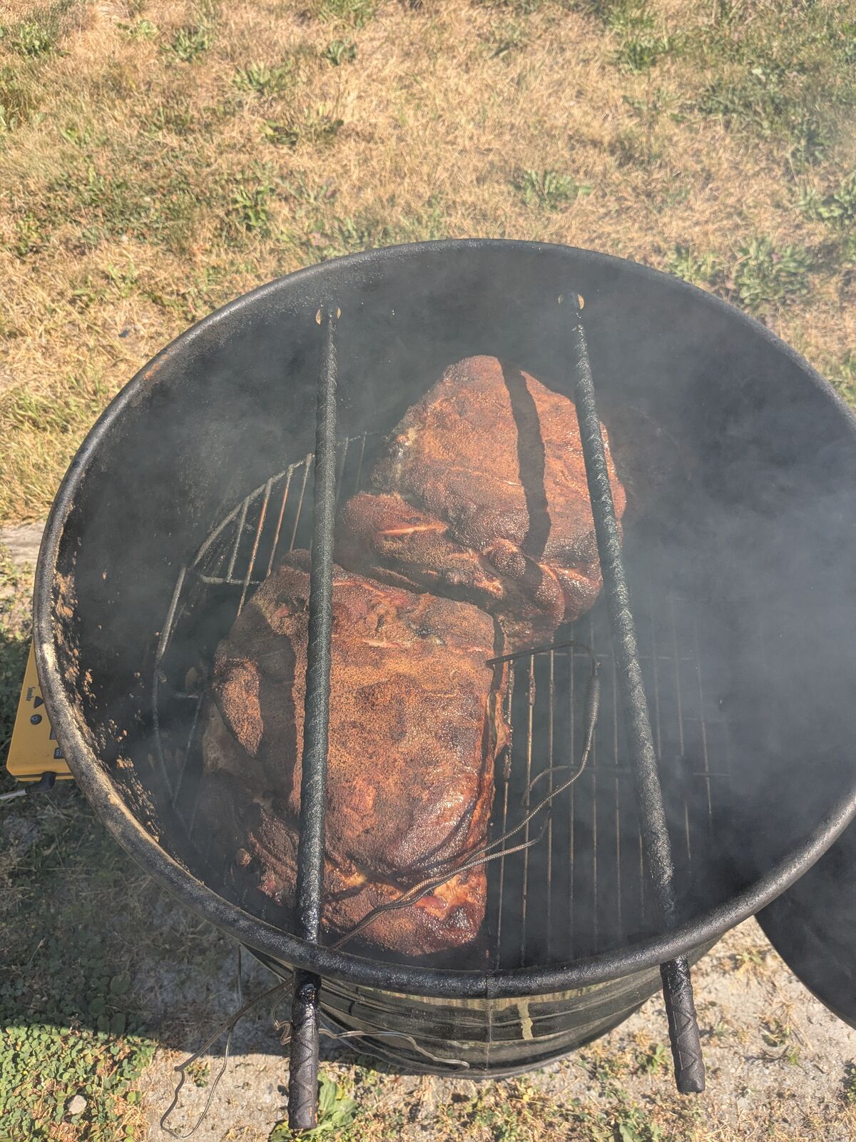 Looking down into the open Pit Barrel Cooker: two pork shoulders with deep mahogany bark on the grate, smoke drifting across.